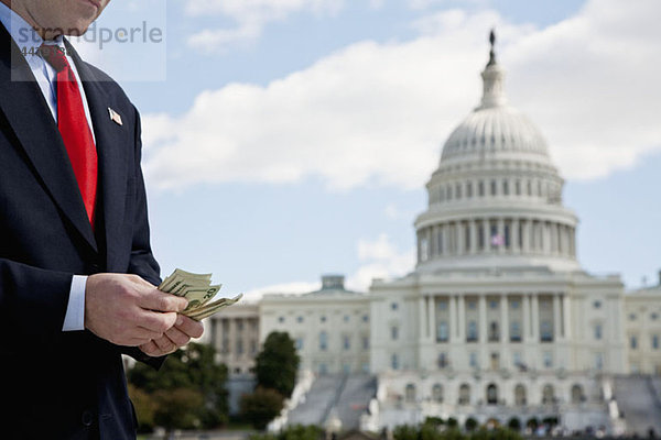 Ein Politiker  der vor dem US Capitol Building Geld zählt.