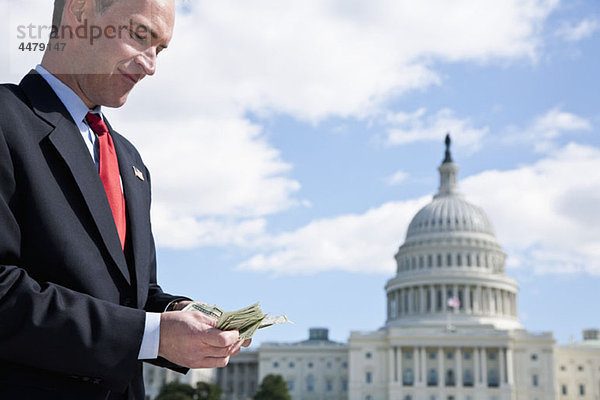 Ein Politiker  der vor dem US Capitol Building Geld zählt.