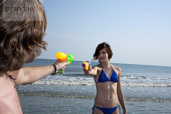 Ein junges Paar spielt am Strand mit Spritzpistolen.