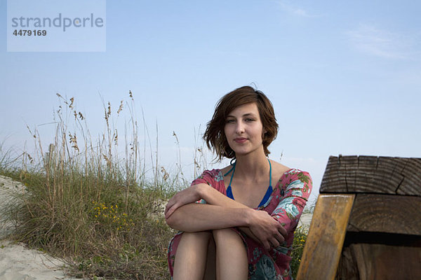 Eine junge Frau sitzt im Sand am Strand.