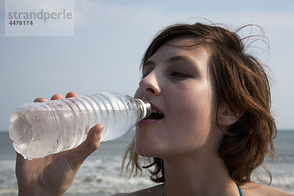 Eine Frau  die Wasser in Flaschen am Strand trinkt.