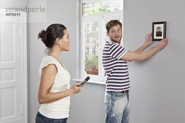 Ein Paar hängt einen Bilderrahmen in seinem neuen Zuhause auf.