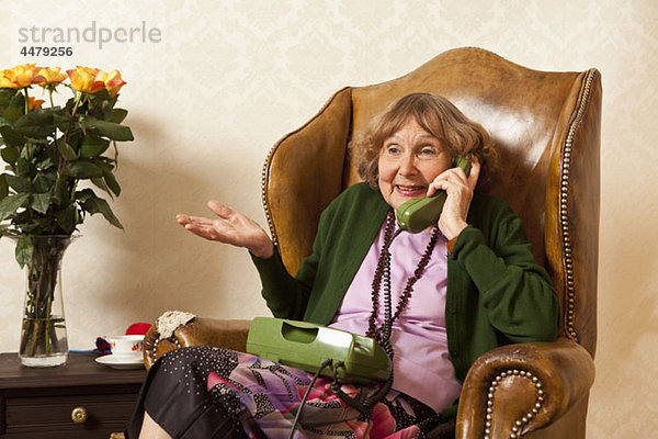 Eine ältere Frau  die in ihrem Wohnzimmer telefoniert.