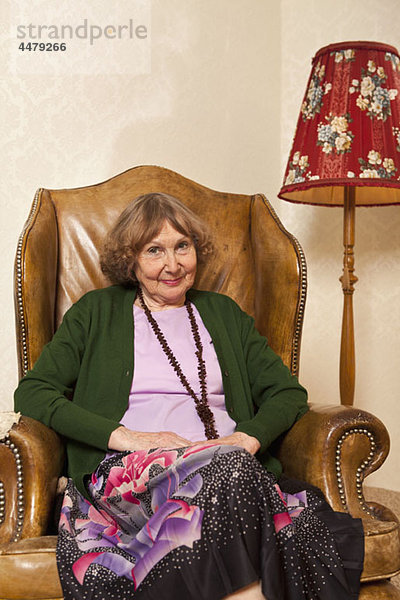 Eine ältere Frau sitzt in einem Sessel in ihrem Wohnzimmer.