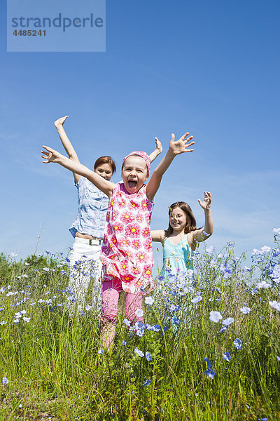 Mutter und zwei Töchter laufen über eine Blumenwiese