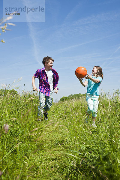 Zwei Kinder laufen mit Ball über eine Wiese