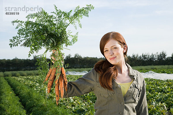 Junge Frau hält einen Haufen Karotten auf dem Feld