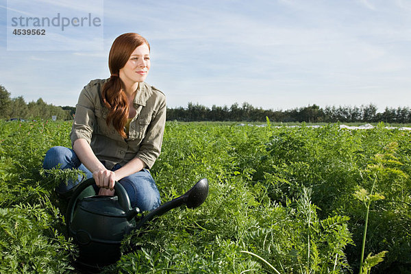 Frau beim Gießen von Getreide auf dem Feld mit Gießkanne