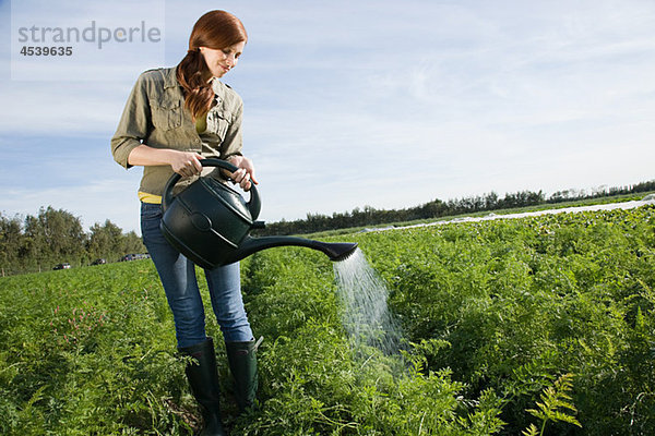Frau beim Gießen von Getreide auf dem Feld mit Gießkanne