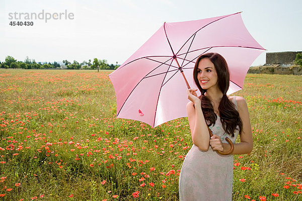 Junge Frau im Mohnfeld mit rosa Sonnenschirm