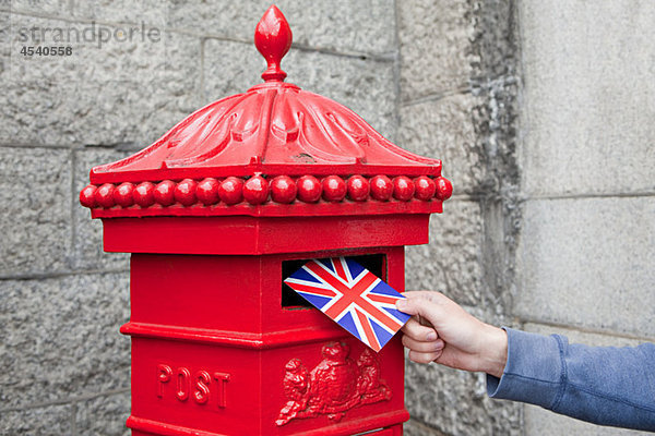 Person  die Postkarte in den Briefkasten legt  London