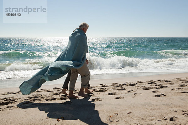 Ein reifes Paar  das am Strand spazieren geht und in eine Decke gehüllt ist.