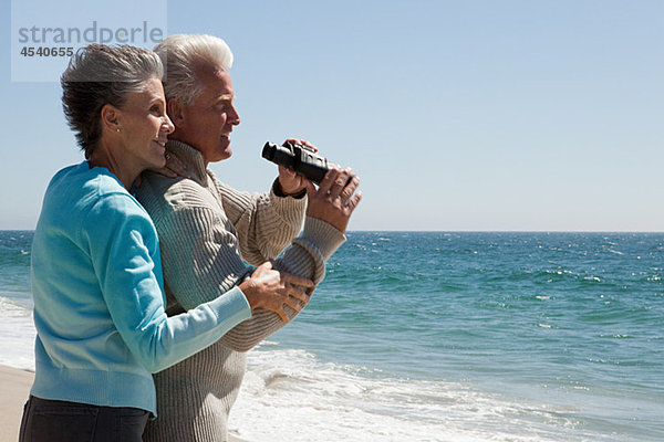 Erwachsenes Paar am Strand mit Fernglas