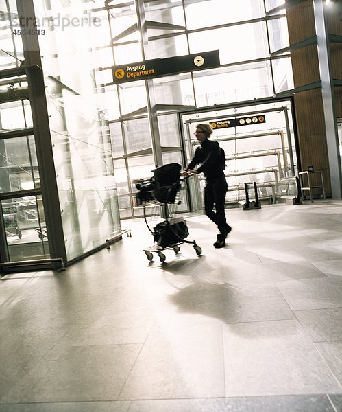 Frau drängen Gepäckwagen am Flughafen