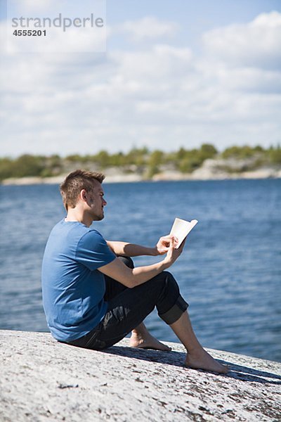 Mitte erwachsenen Männern am Strand sitzen und lesen Buch