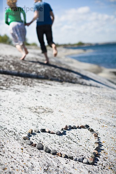 Pebbles in Form von Herzen am Strand  Paar im Hintergrund laufen