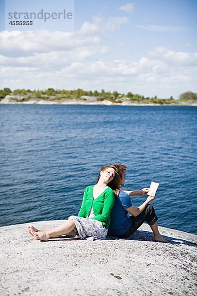 Mitte adult paar am Strand sitzen und wegsehen  Mann Buch zu lesen
