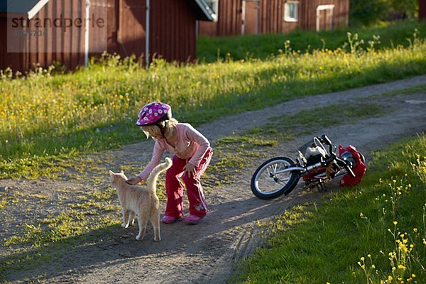 Mädchen streicheln Katze in der Nähe von Fahrrad im Dorf
