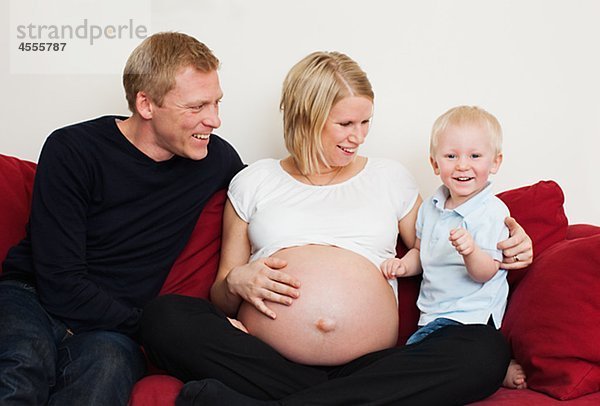 Schwangere Frau mit Partner und Sohn auf Sofa sitzen und lächelnd