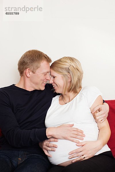 Mann mit schwangere Frau sitzt auf Sofa und suchen einander