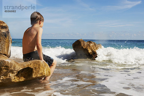 Junge sitzt auf einem Felsen und schaut aufs Meer.