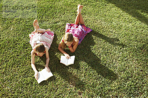 Mädchen  die auf Gras liegen und Bücher lesen