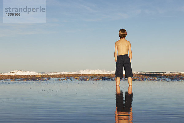 Junge und Reflektion am Strand stehend