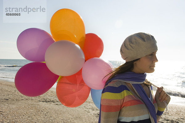 Preteen Mädchen mit einem Haufen Luftballons  die am Strand laufen.