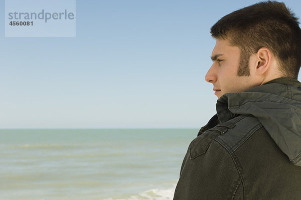 Junger Mann am Strand betrachtet nachdenklich die Aussicht