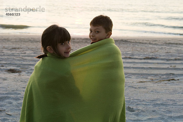 Kinder zusammen in eine Decke am Strand gewickelt