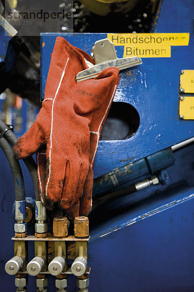 Arbeitshandschuhe gebeizt mit Bitumen an der Maschine in der Teppichfliesenfabrik