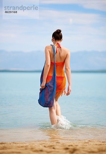 Kroatien  Zadar  Junge Frau beim Spaziergang im Wasser am Strand