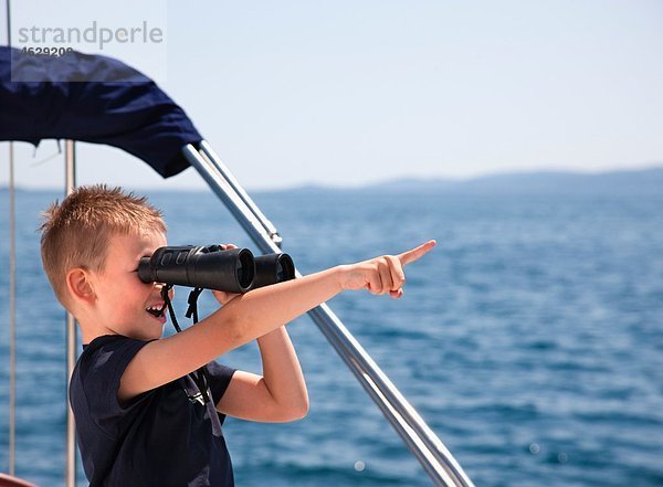 Kroatien  Zadar  Junge sucht durch ein Fernglas vom Segelboot aus