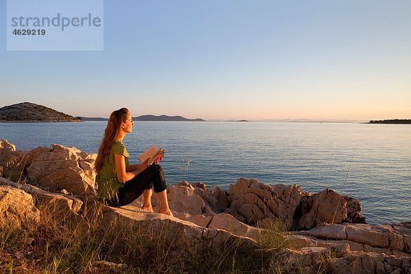 Kroatien  Zadar  Junge Frau mit Buch mit Blick auf den Strand