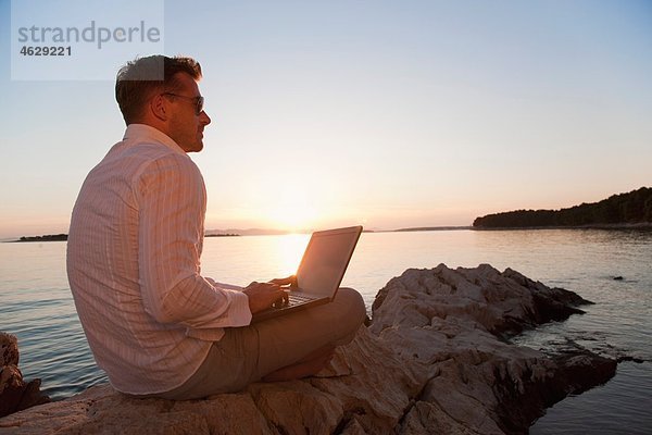 Kroatien  Zadar  Junger Mann mit Laptop am Strand