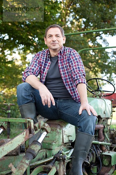 Erwachsener Mann auf Traktor sitzend  lächelnd  Portrait