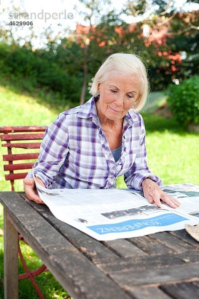 Seniorin beim Zeitungslesen auf dem Bauernhof.