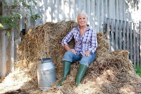 Seniorin auf Gras sitzend mit Milchkanne