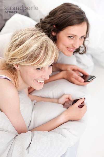 Junge Frauen im Bett mit Handy  lächelnd