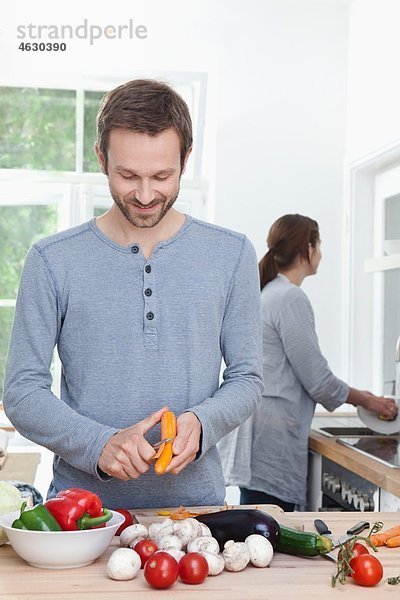 Mann schält Karotte in der Küche  Frau im Hintergrund