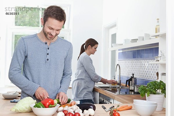 Mann hackt Zucchini in der Küche  Frau im Hintergrund