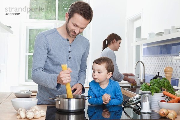 Deutschland  Bayern  München  Vater und Sohn (2-3 Jahre) kochen Spaghetti und Mutter im Hintergrund
