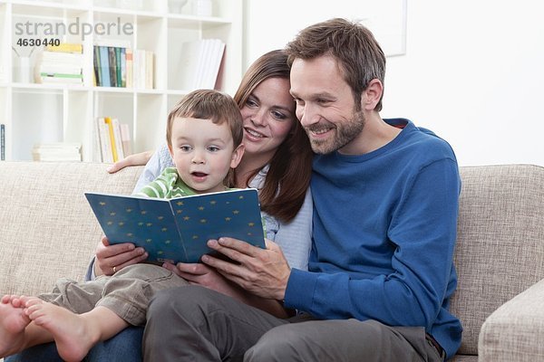 Deutschland  Bayern  München  Eltern Lesebuch mit Sohn (2-3 Jahre) im Wohnzimmer