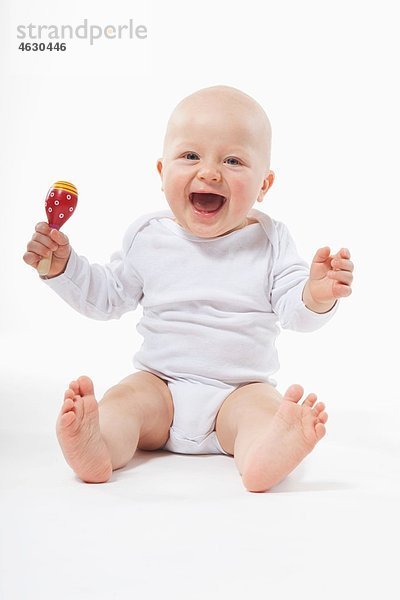 Baby Junge (6-11 Monate) hält Rassel  lächelnd