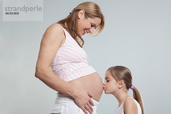 Tochter küssend auf den Bauch ihrer schwangeren Mutter