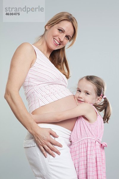 Tochter umarmt schwangere Mutter  lächelnd  Portrait