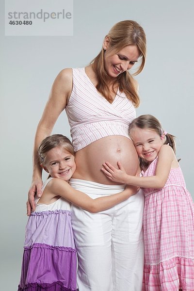 Töchter  die schwangere Mutter umarmen  lächelnd