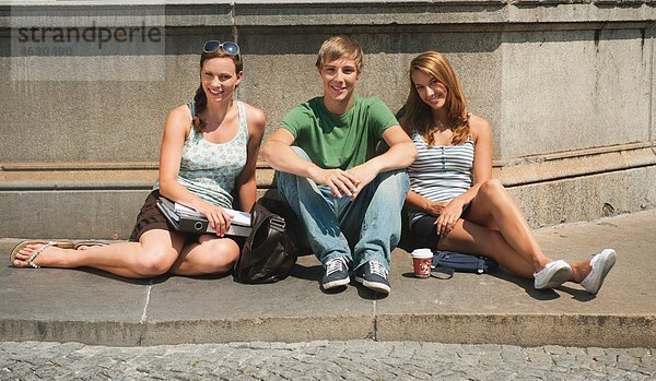 Junger Mann und junge Frauen sitzen am Brunnen der Universität