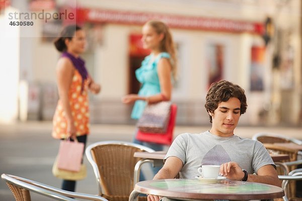 Junger Mann wartet im Café mit Freunden im Hintergrund