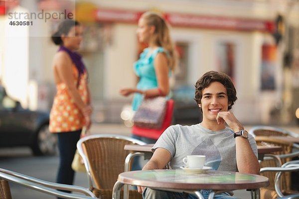 Junger Mann im Café lächelt mit Freunden im Hintergrund
